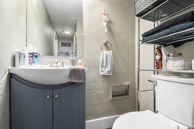 half bath with toilet, a textured wall, and vanity