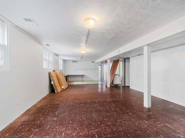 basement featuring visible vents, a textured ceiling, tile patterned floors, and concrete block wall