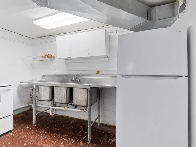 kitchen with freestanding refrigerator, white cabinetry, and range