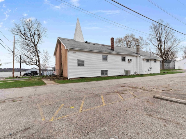 rear view of property featuring central air condition unit, a chimney, and uncovered parking