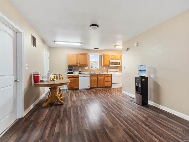 kitchen featuring a sink, white appliances, light countertops, baseboards, and dark wood-type flooring