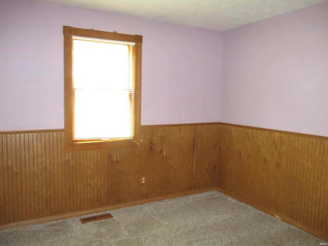 carpeted spare room featuring visible vents, wainscoting, and plenty of natural light