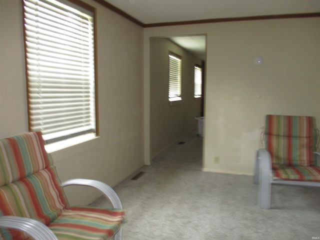 sitting room with baseboards, light colored carpet, ornamental molding, and visible vents