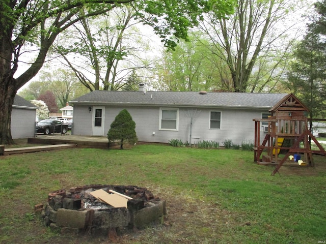 rear view of house with a lawn, a chimney, a playground, and an outdoor fire pit