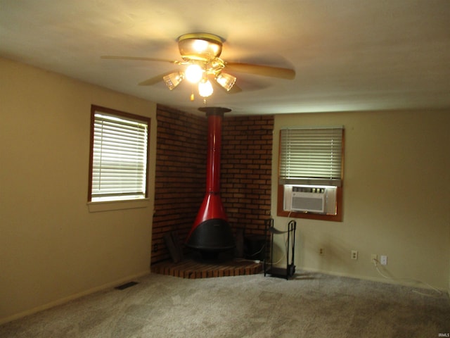 carpeted spare room with visible vents, a wood stove, baseboards, ceiling fan, and cooling unit