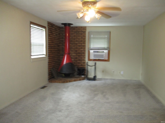 carpeted empty room featuring ceiling fan, visible vents, a wood stove, and cooling unit