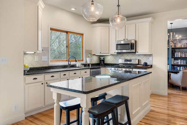 kitchen with a sink, light wood finished floors, appliances with stainless steel finishes, and white cabinetry