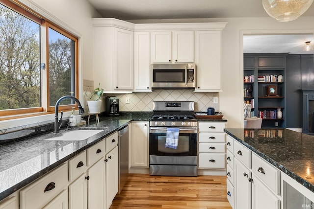 kitchen with backsplash, appliances with stainless steel finishes, light wood-type flooring, a sink, and white cabinets