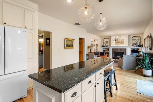kitchen featuring light wood-style floors, a center island, freestanding refrigerator, white cabinetry, and visible vents