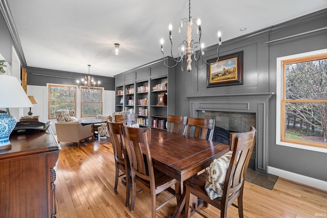dining space featuring an inviting chandelier, crown molding, a fireplace, baseboards, and light wood-style flooring
