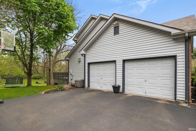 garage featuring central AC unit, a trampoline, and aphalt driveway