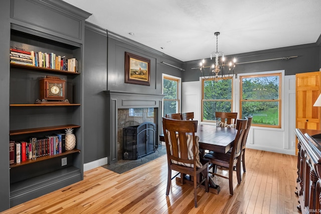 dining room featuring an inviting chandelier, ornamental molding, built in shelves, a tile fireplace, and light wood finished floors