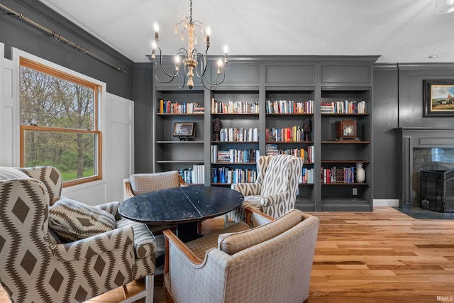 sitting room featuring crown molding, built in features, wood finished floors, a fireplace, and a notable chandelier