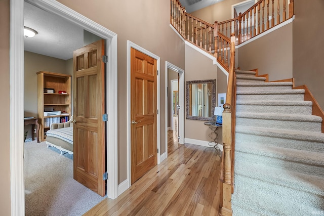 staircase with baseboards, a high ceiling, and wood finished floors