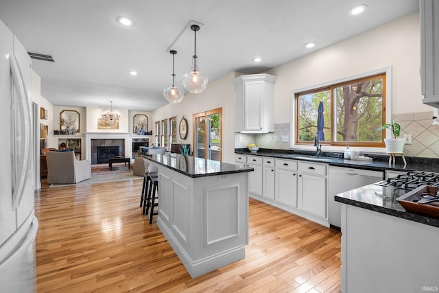 kitchen featuring visible vents, freestanding refrigerator, open floor plan, dishwashing machine, and white cabinets