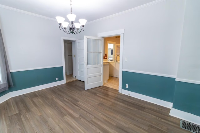 unfurnished dining area with crown molding, an inviting chandelier, wood finished floors, and visible vents