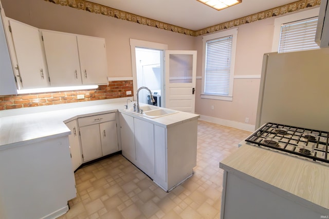 kitchen with freestanding refrigerator, a peninsula, a sink, and light countertops