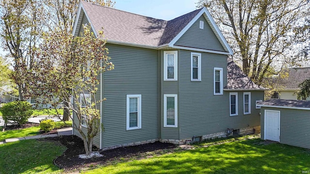 rear view of house featuring a lawn, an outdoor structure, a storage unit, and a shingled roof