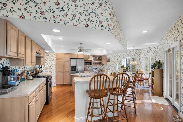 kitchen featuring light wood-style floors, light countertops, stainless steel appliances, wallpapered walls, and a kitchen bar