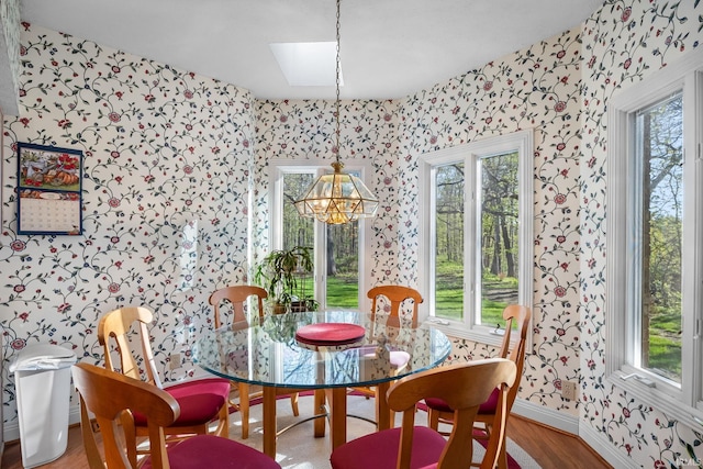 dining space featuring a skylight, wood finished floors, baseboards, a notable chandelier, and wallpapered walls