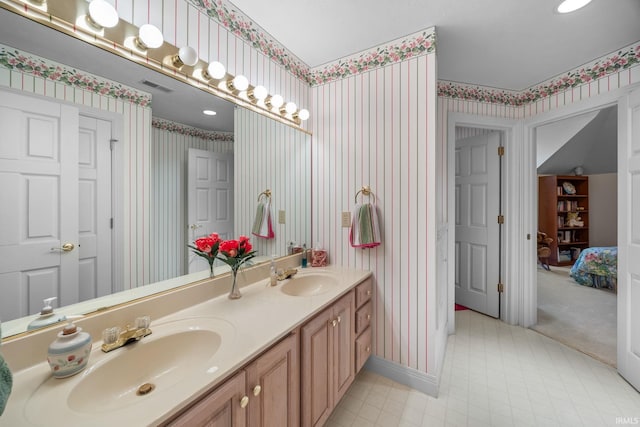 bathroom with visible vents, a sink, double vanity, and wallpapered walls