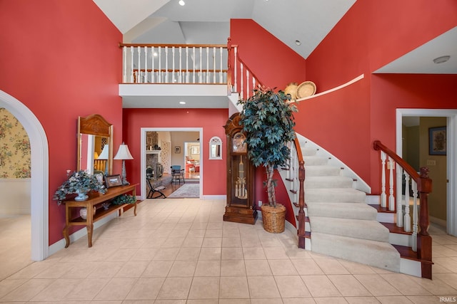 stairway with high vaulted ceiling, baseboards, tile patterned floors, and arched walkways