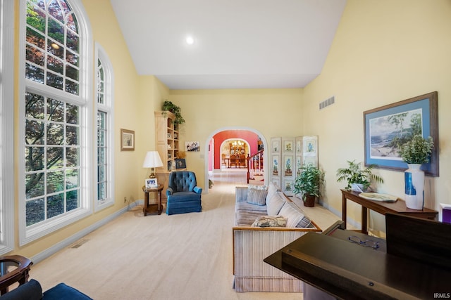 carpeted living room with visible vents, arched walkways, plenty of natural light, and high vaulted ceiling