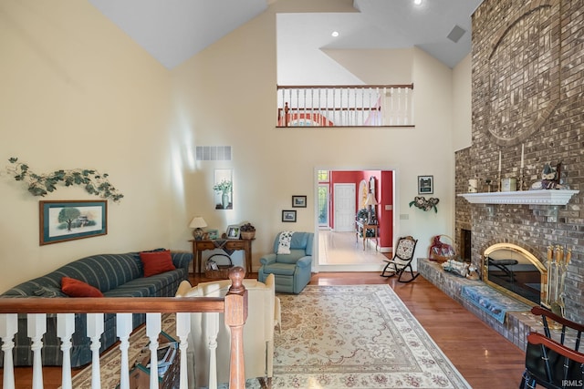 living area with high vaulted ceiling, a brick fireplace, wood finished floors, and visible vents
