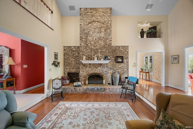living area featuring a high ceiling, a fireplace, baseboards, wood finished floors, and visible vents