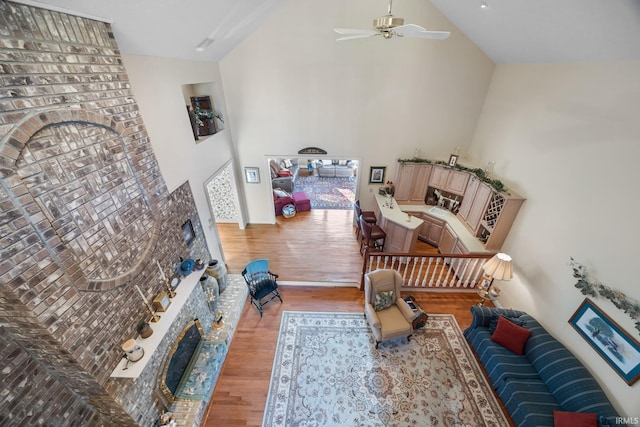 living room featuring a ceiling fan, high vaulted ceiling, light wood finished floors, and a fireplace