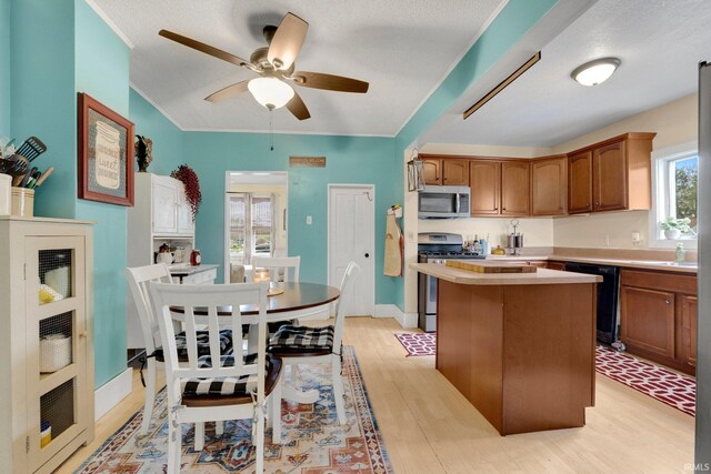 kitchen with ceiling fan, a kitchen island, light countertops, stainless steel appliances, and light wood-style flooring