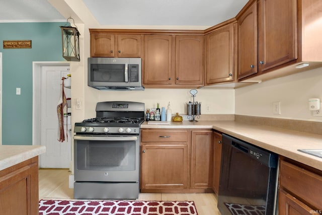 kitchen featuring light countertops, light wood finished floors, appliances with stainless steel finishes, and brown cabinets