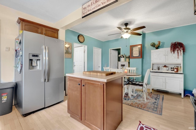 kitchen with light wood finished floors, light countertops, a center island, a ceiling fan, and stainless steel refrigerator with ice dispenser