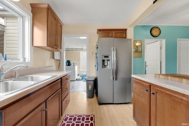 kitchen with stainless steel fridge, a sink, light wood finished floors, and light countertops