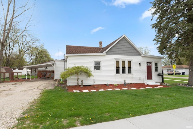 view of front facade featuring a shingled roof, a front lawn, a chimney, a carport, and driveway