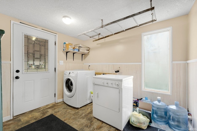 laundry area with laundry area, wainscoting, a textured ceiling, wood walls, and washing machine and dryer