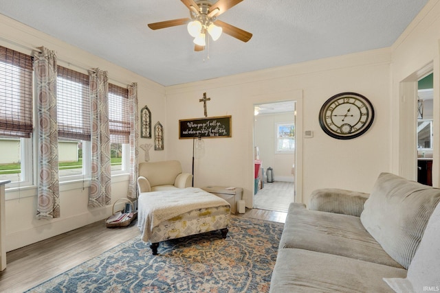living area featuring baseboards, a textured ceiling, ceiling fan, and wood finished floors