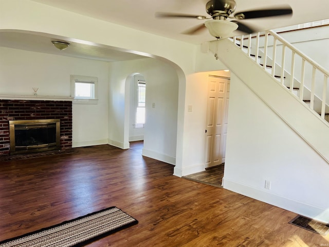 unfurnished living room with a ceiling fan, arched walkways, visible vents, and wood finished floors