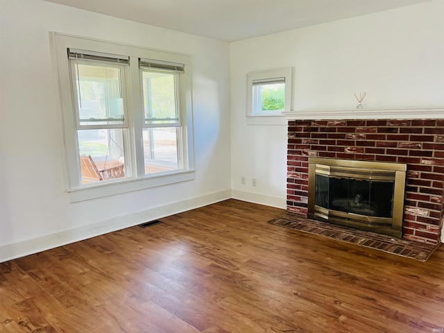 unfurnished living room featuring a brick fireplace, baseboards, visible vents, and wood finished floors