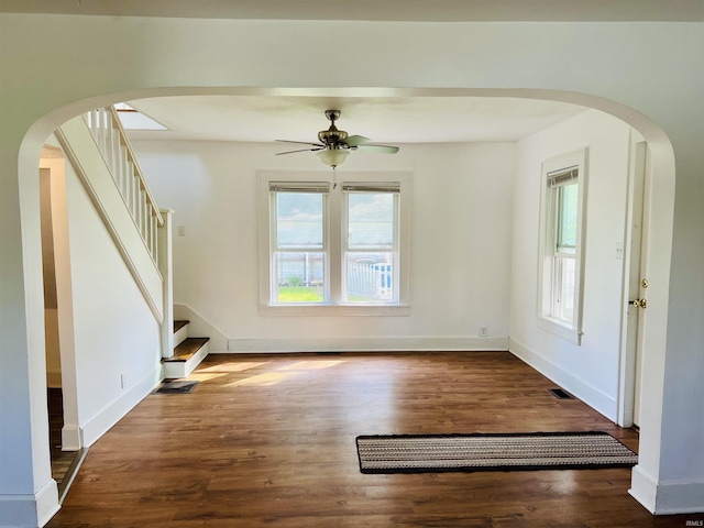 unfurnished living room featuring stairway, arched walkways, ceiling fan, and wood finished floors