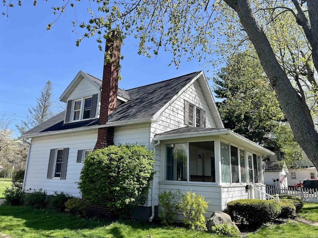 view of property exterior with a lawn, a chimney, a sunroom, and a shingled roof