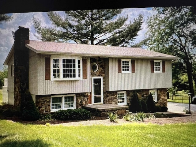 raised ranch with a front yard, stone siding, and a chimney