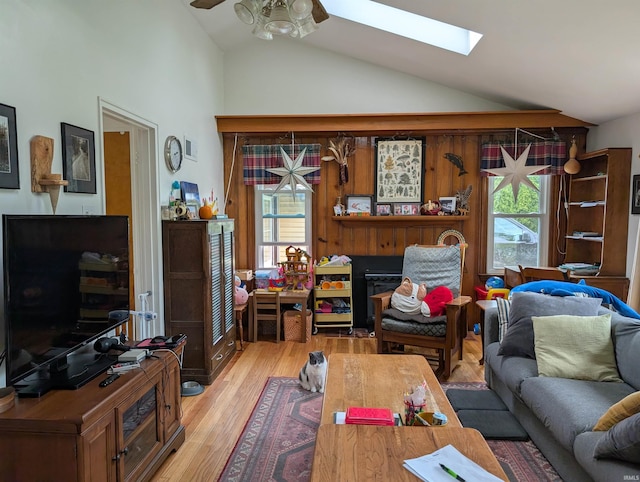 living area with a skylight, high vaulted ceiling, a ceiling fan, and light wood-style flooring