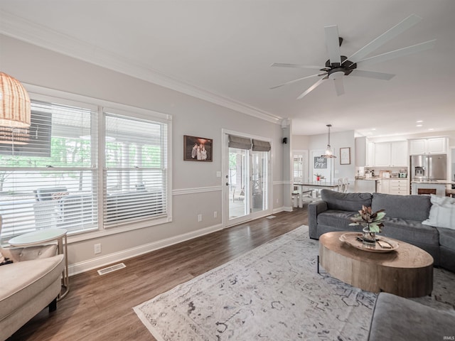 living room featuring visible vents, crown molding, wood finished floors, baseboards, and ceiling fan