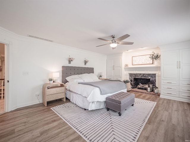 bedroom with ceiling fan, light wood-style flooring, a high end fireplace, visible vents, and ornamental molding