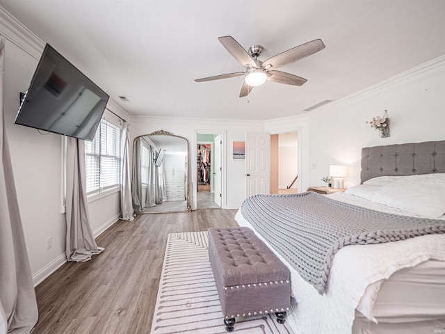 bedroom featuring ornamental molding, baseboards, a walk in closet, a ceiling fan, and light wood finished floors
