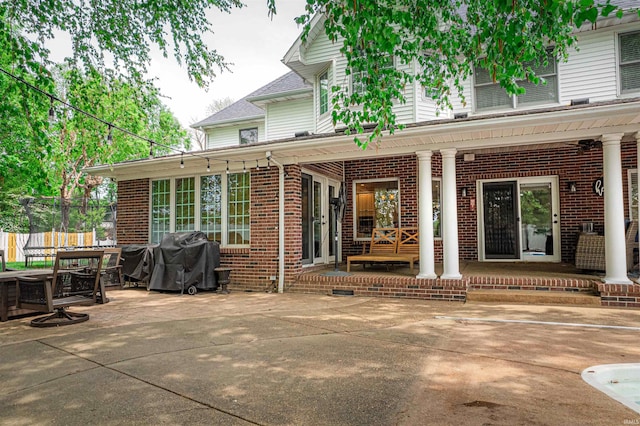 rear view of house with brick siding, a patio area, fence, and covered porch