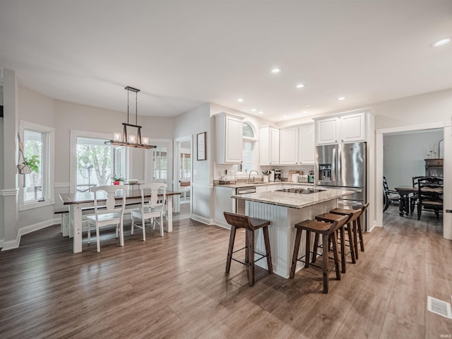 kitchen featuring white cabinets, a sink, wood finished floors, a kitchen island, and stainless steel refrigerator with ice dispenser