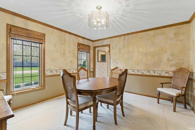 carpeted dining area featuring an inviting chandelier, baseboards, crown molding, and a wainscoted wall