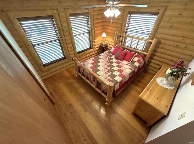 bedroom featuring a ceiling fan, rustic walls, wood finished floors, and multiple windows